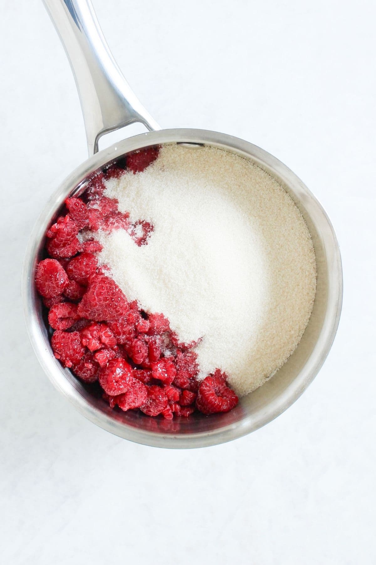 Frozen raspberries and sugar in a saucepan before cooking homemade chocolate raspberry jam.