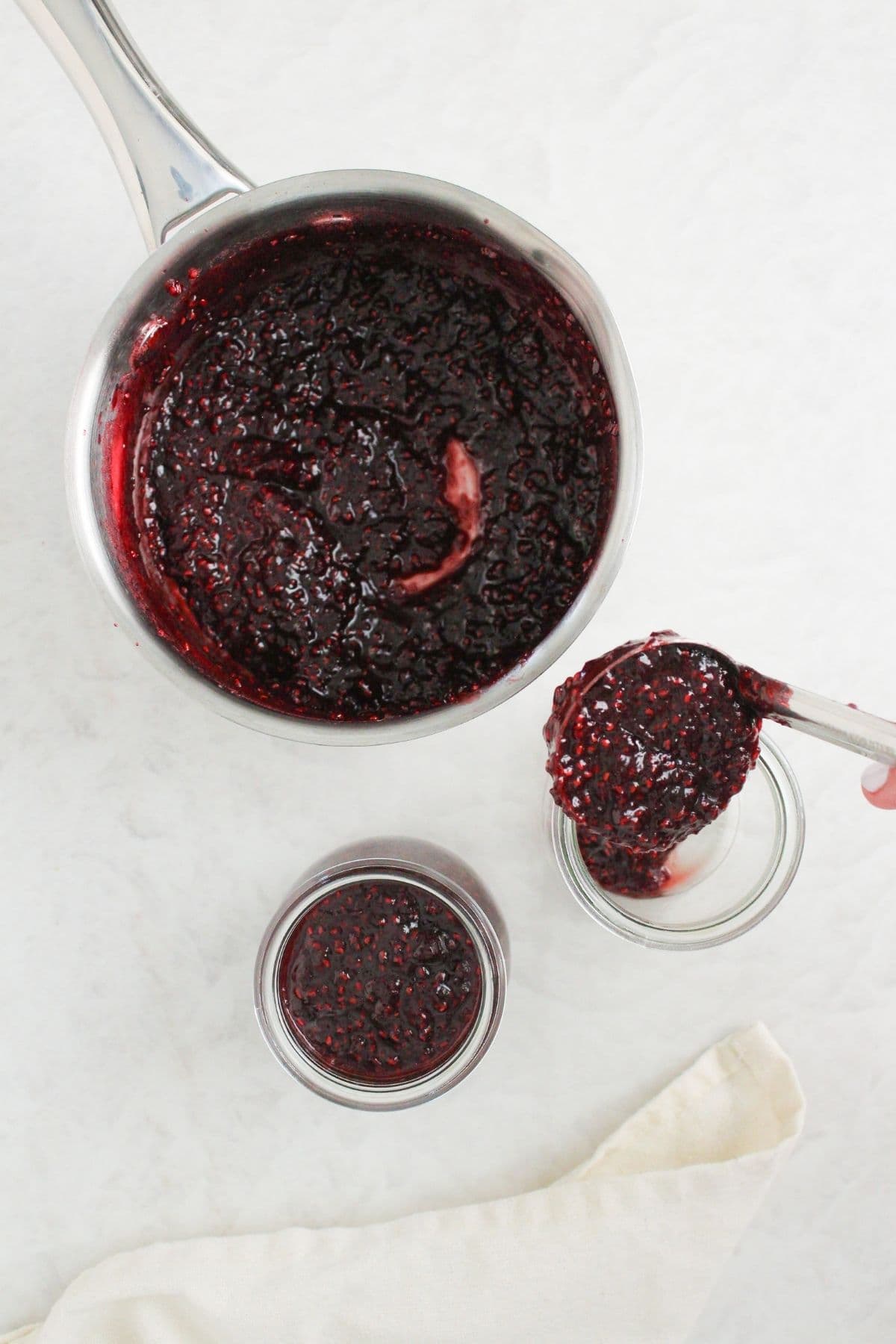 Homemade chocolate raspberry jam being ladled from a saucepan into clean glass jars.
