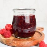 Jar of homemade chocolate raspberry jam served with fresh raspberries on a wooden board.