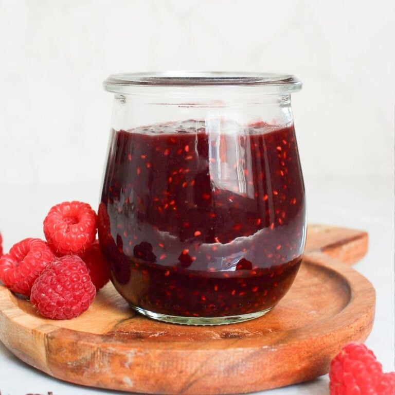 Jar of homemade chocolate raspberry jam served with fresh raspberries on a wooden board.