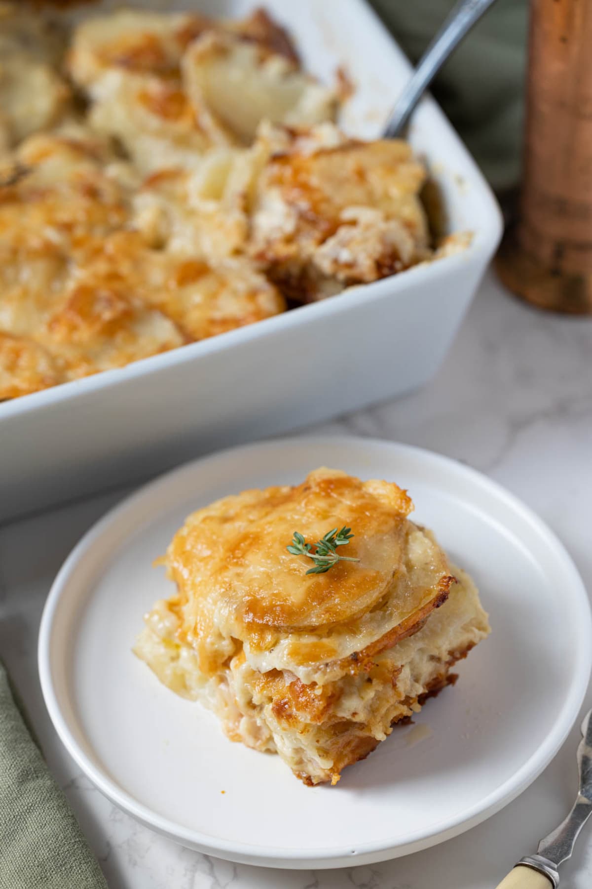 A serving of sourdough au gratin potatoes on a plate with the baking dish behind it.