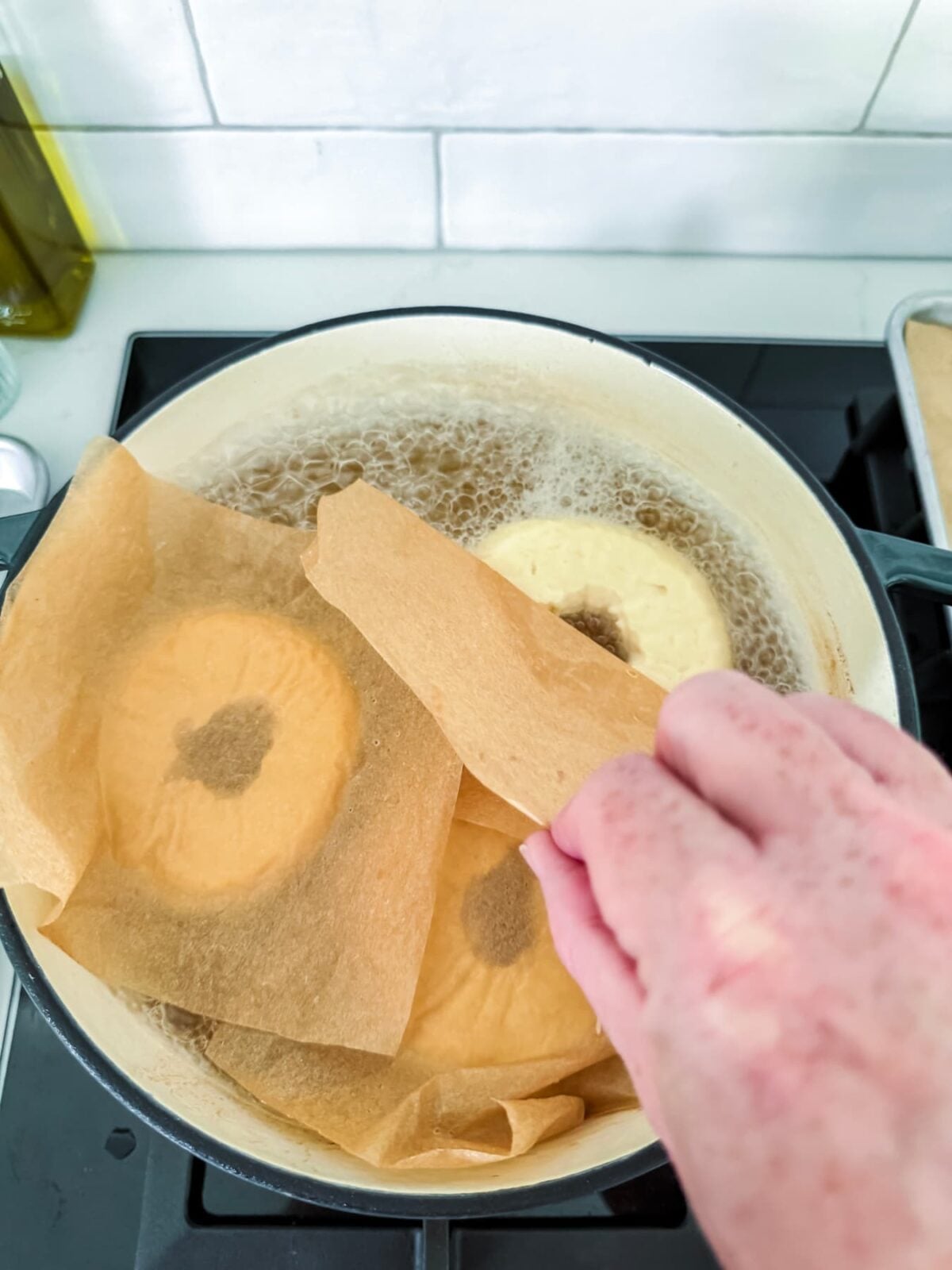 Using parchment paper to gently lower homemade sourdough bagels into boiling water before baking for a chewy crust.