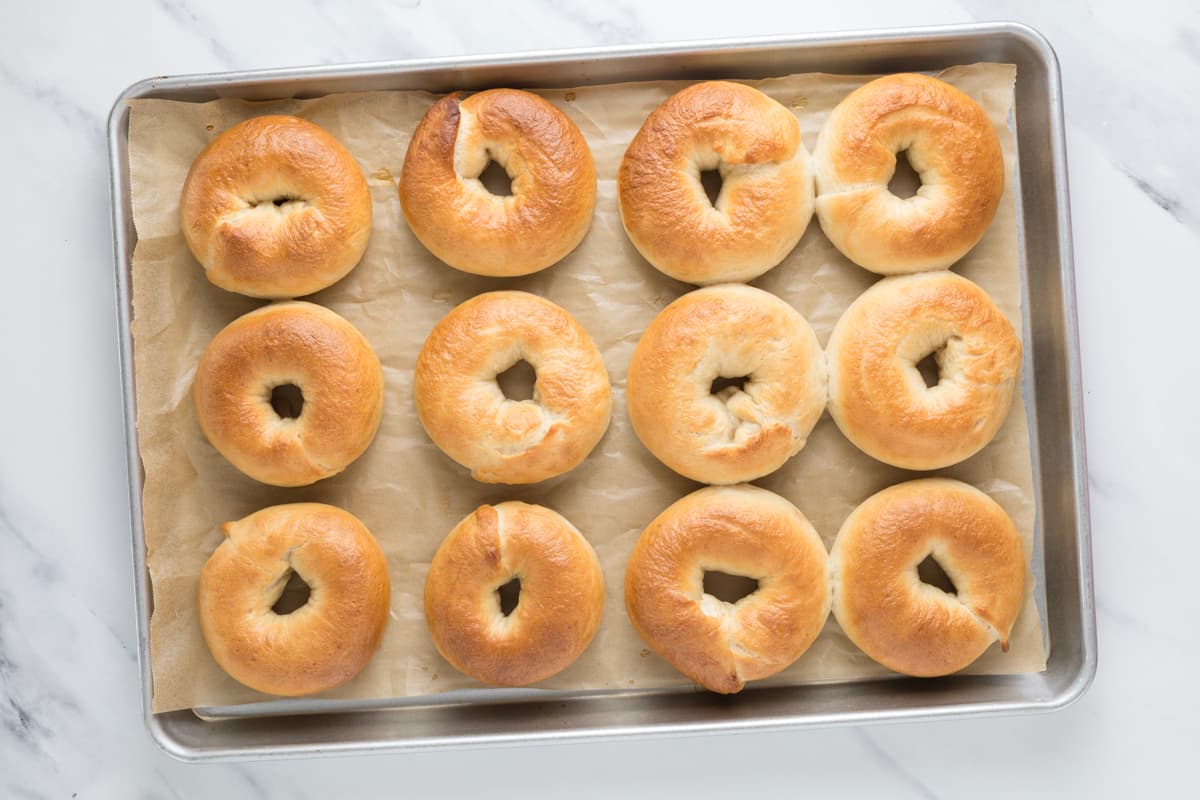 Freshly baked sourdough bagels cooling on a baking sheet with their classic chewy crust and golden finish.
