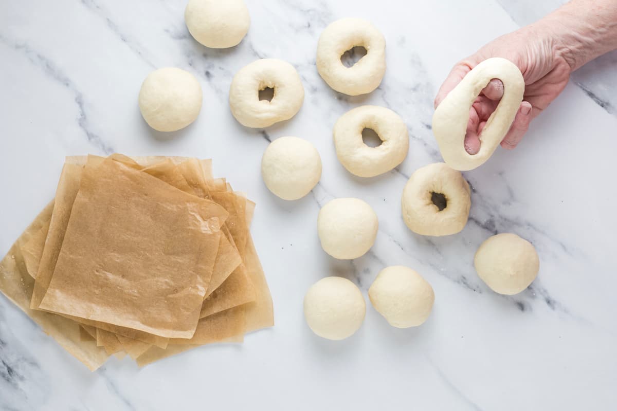 Stretching the hole of a shaped sourdough bagel over two fingers to create a larger center before proofing.