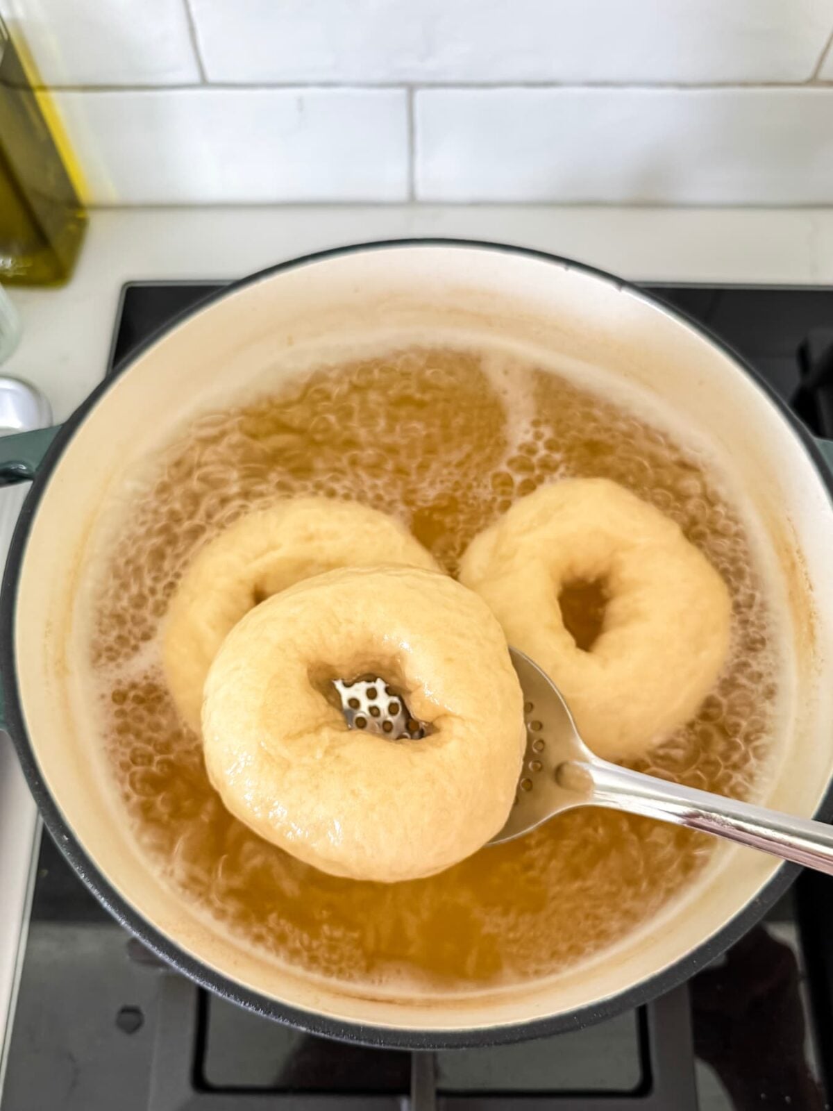 Lifting a boiled sourdough bagel from honey water with a slotted spoon before baking.