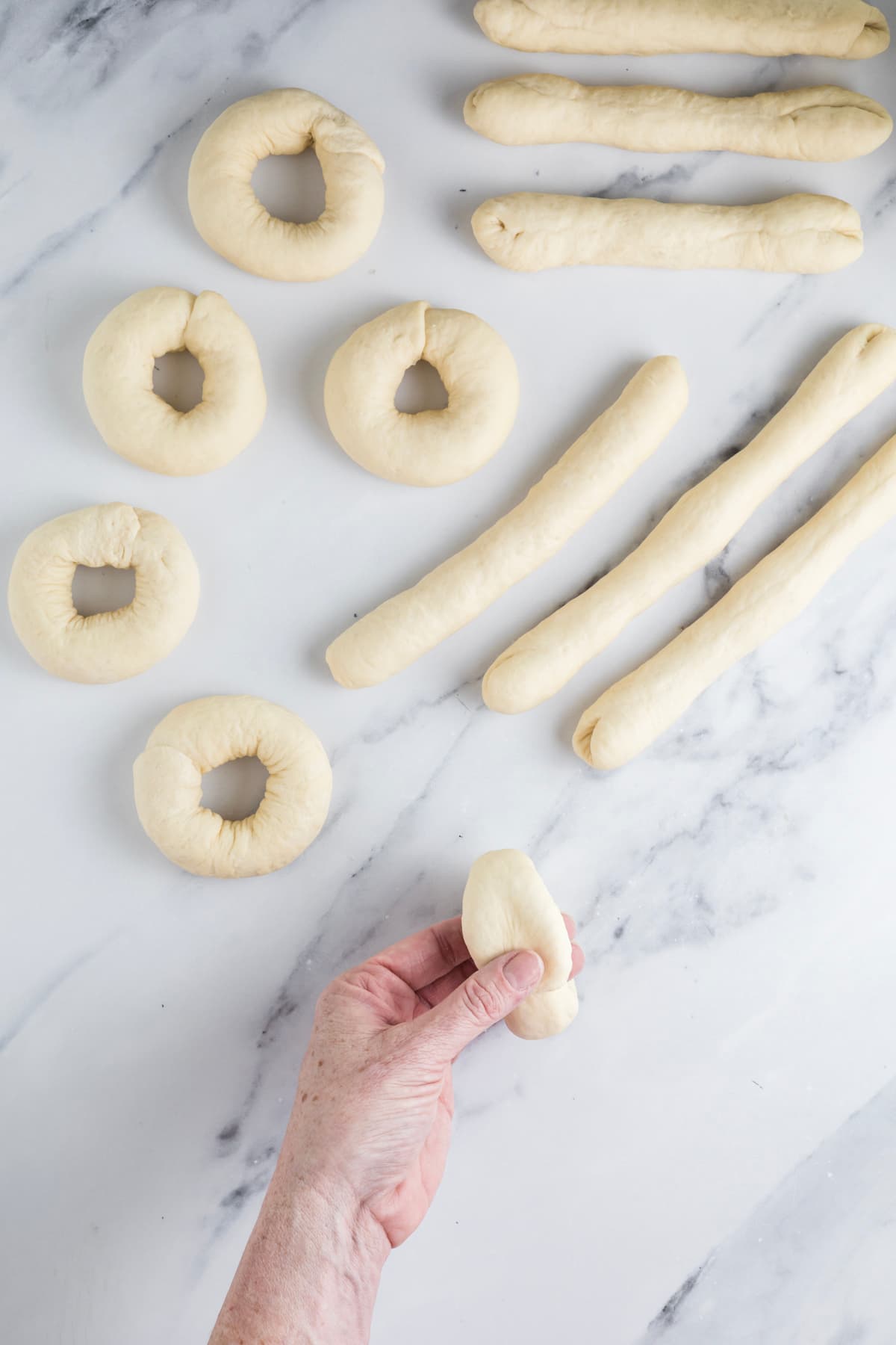 Wrapping a rope of sourdough bagel dough around the hand to begin forming a bagel.