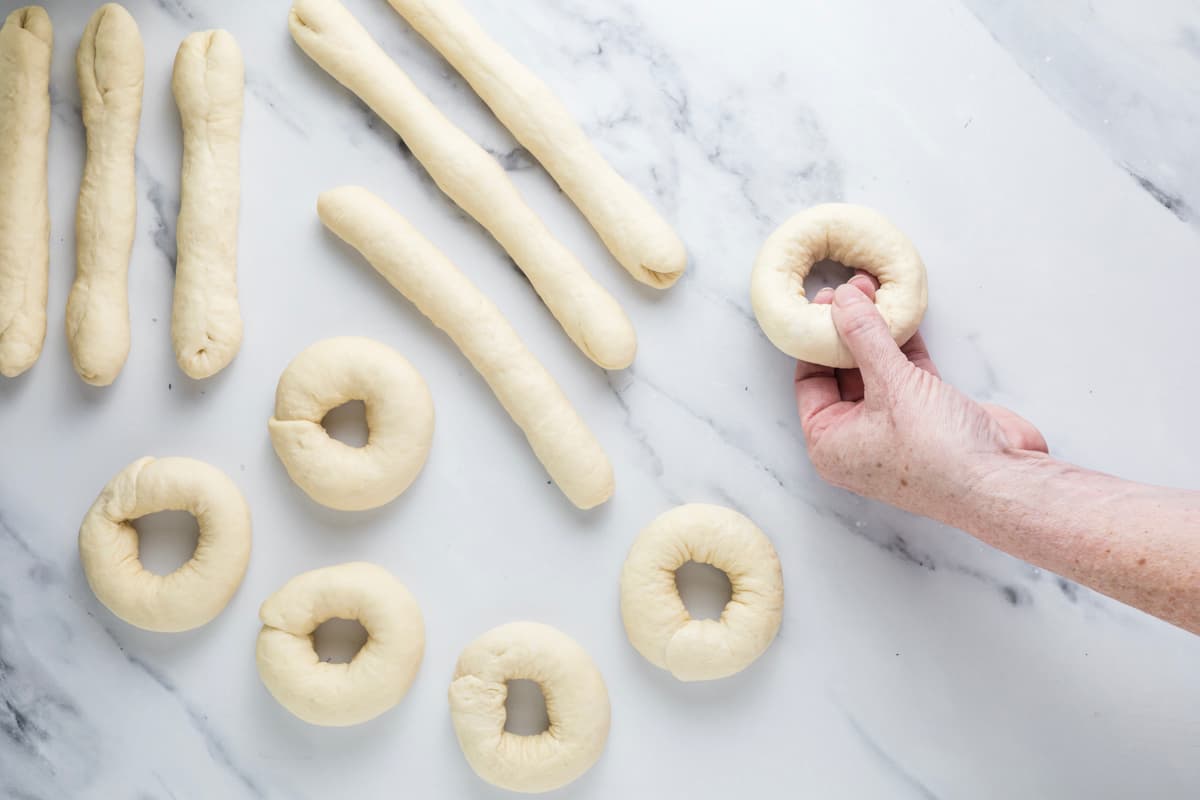 Finished sourdough bagels shaped using the rope method alongside rolled dough ropes.