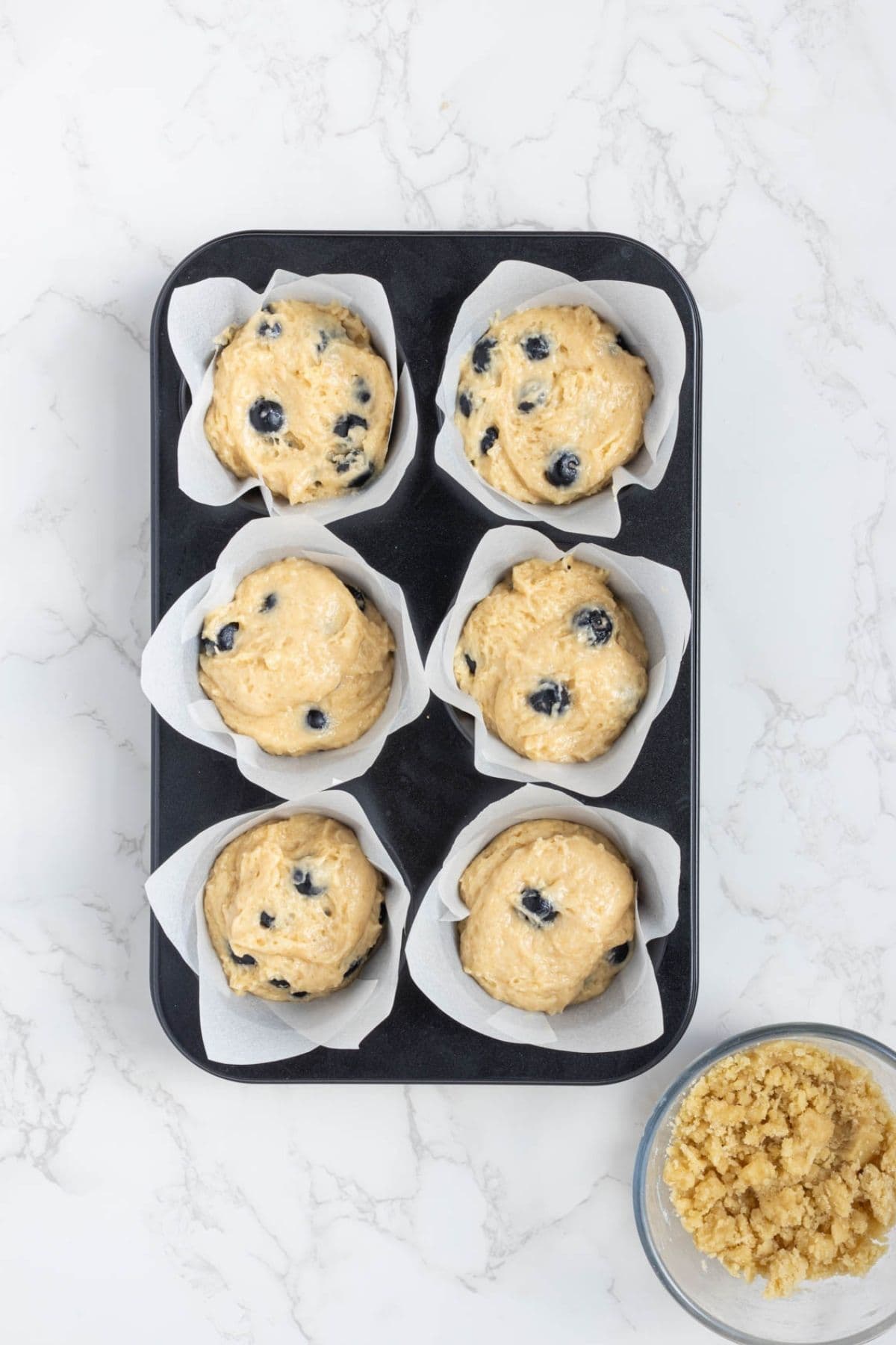 Blueberry muffin batter scooped into parchment-lined muffin cups before adding streusel topping.