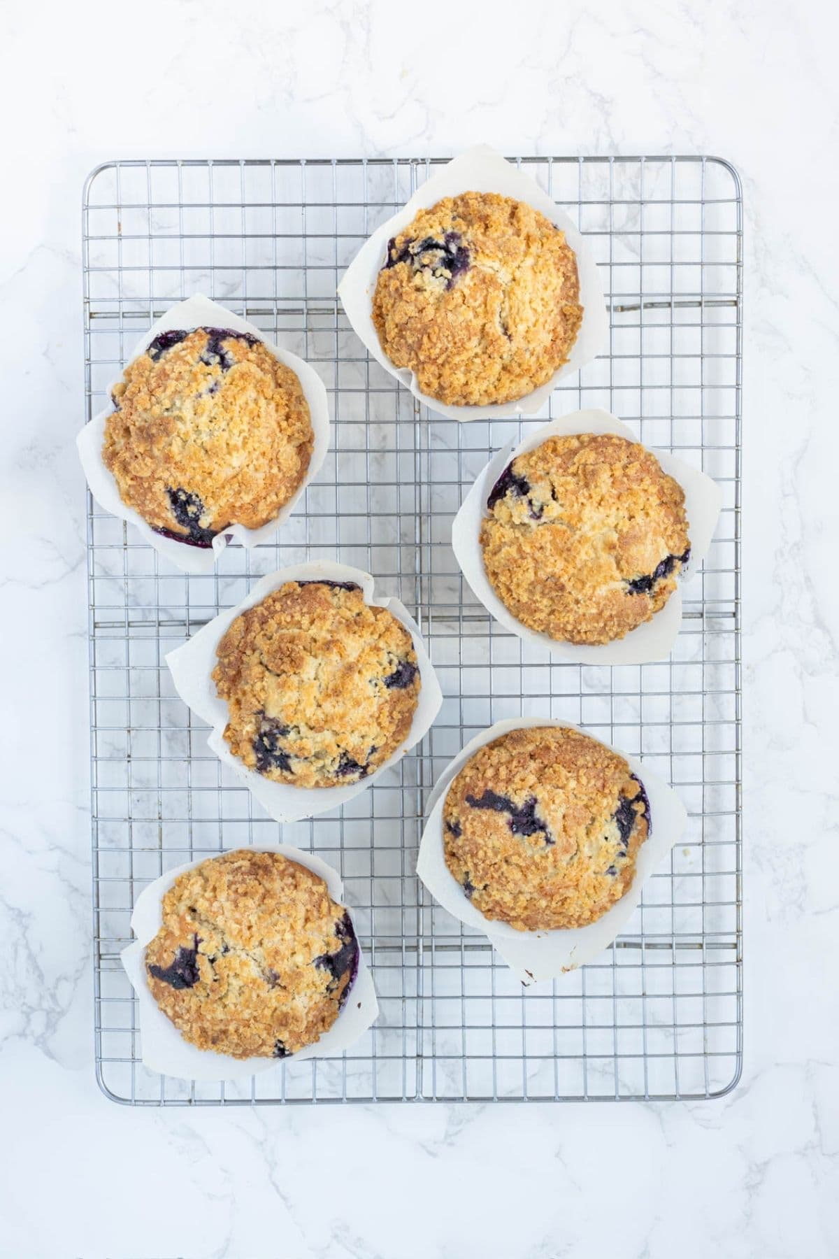 Six sourdough blueberry muffins with streusel topping cooling on a wire rack after baking.