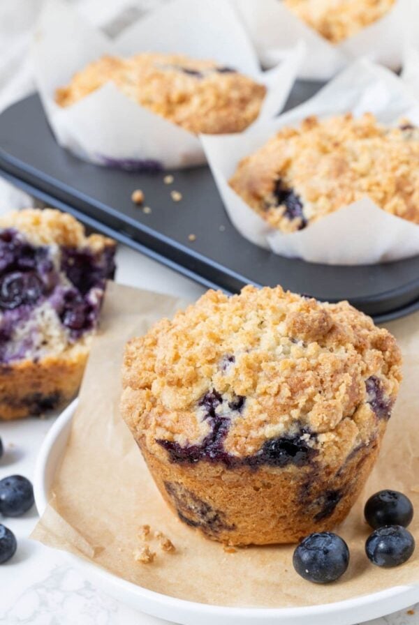 Bakery-style sourdough blueberry muffin with streusel topping served on parchment paper with fresh blueberries.