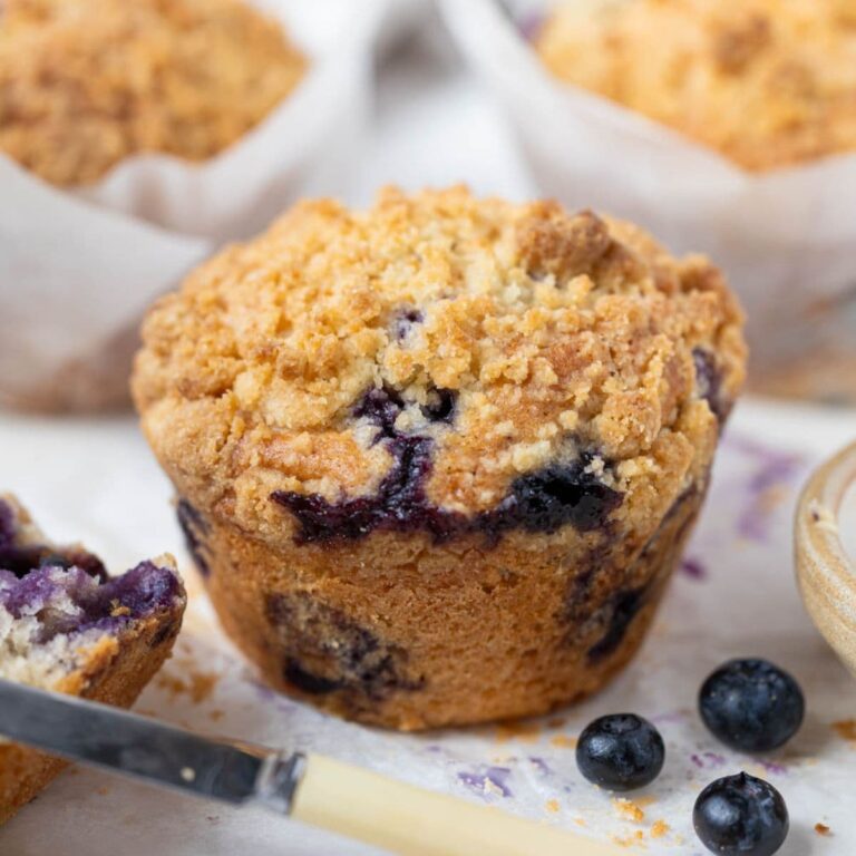 Close up of a sourdough blueberry muffin with crunchy streusel topping and juicy blueberries baked throughout.