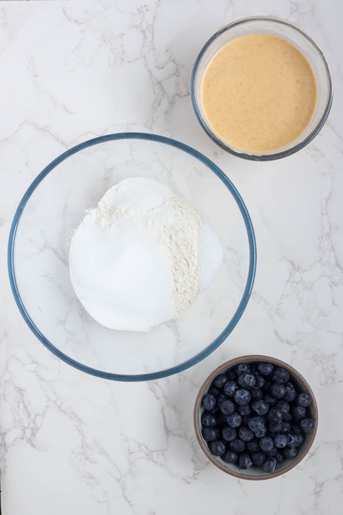 Wet and dry ingredients with the bowl of blueberries ready to mix to make sourdough blueberry muffins with streusel topping.