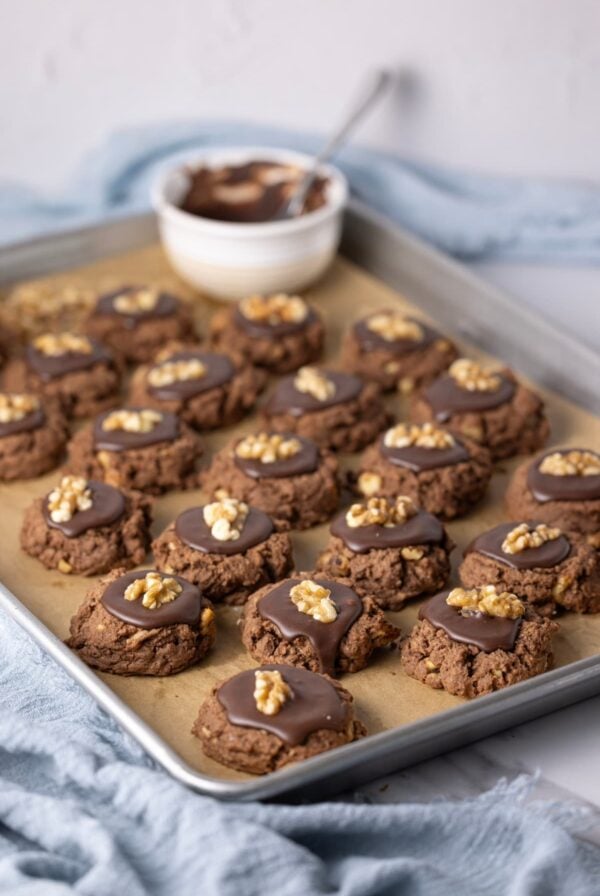 Fresh baked sourdough chocolate walnut cookies on parchment lined baking tray and topped with frosting.