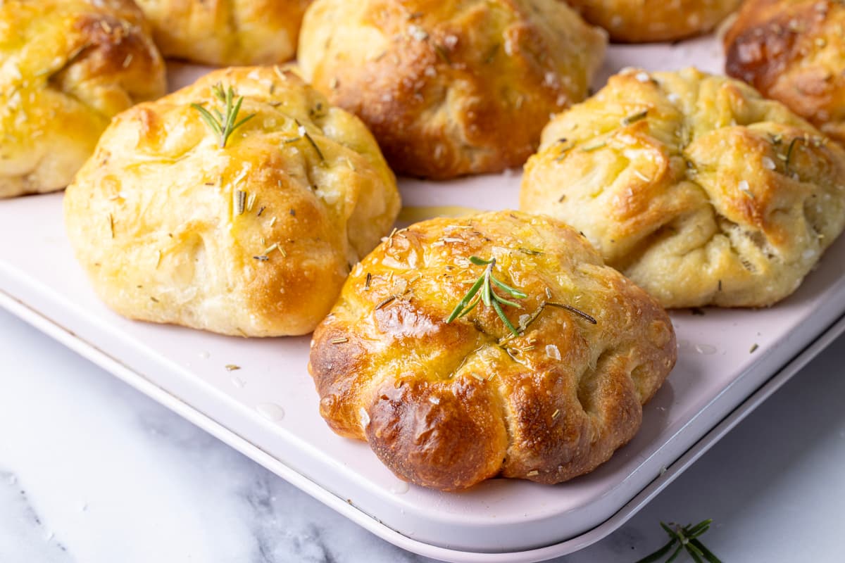 Close-up of baked sourdough focaccia muffins with rosemary and olive oil in a baking pan.
