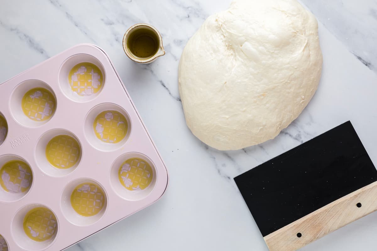 Dividing fermented sourdough focaccia dough into equal portions for muffin cups.