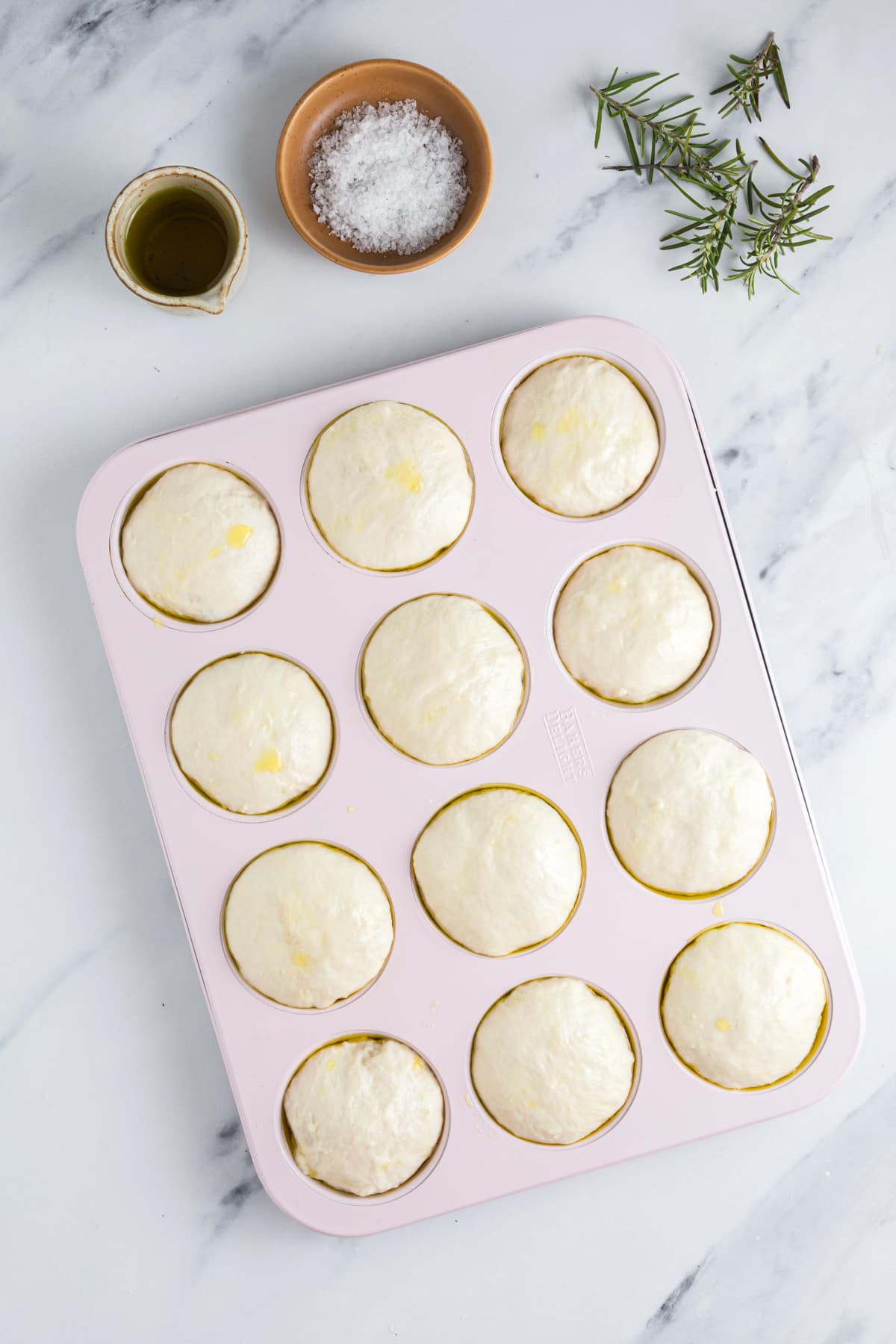 Proofed sourdough focaccia muffin dough risen in a muffin pan before dimpling.