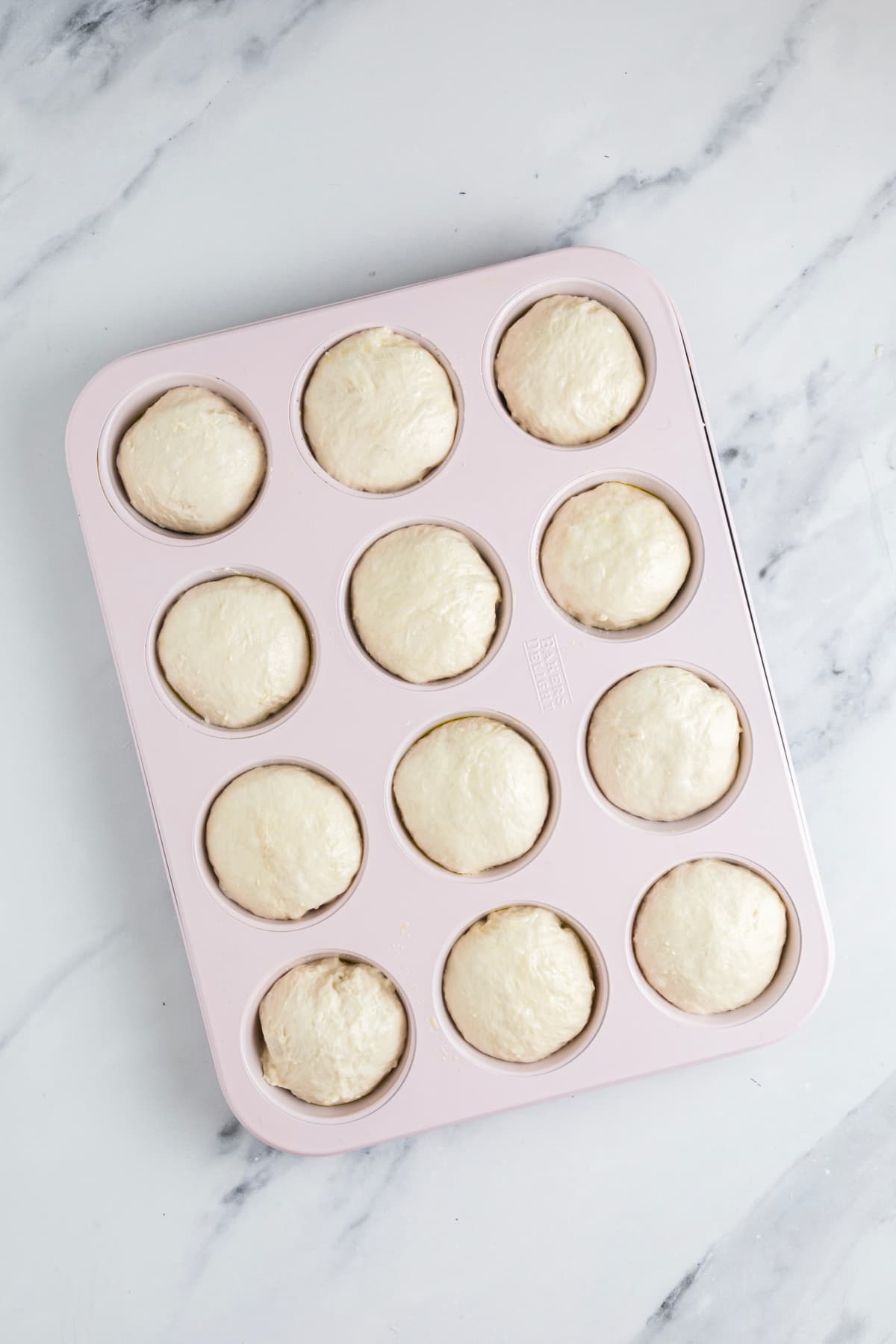 Sourdough focaccia dough balls placed into an oiled muffin pan for proofing.
