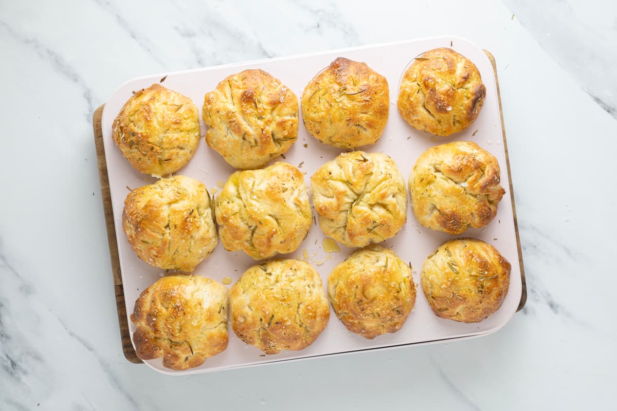 Freshly baked sourdough focaccia muffins cooling in a baking tray after baking.