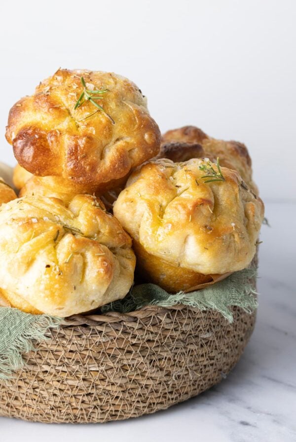 Basket filled with homemade sourdough focaccia muffins topped with rosemary and flaky sea salt.