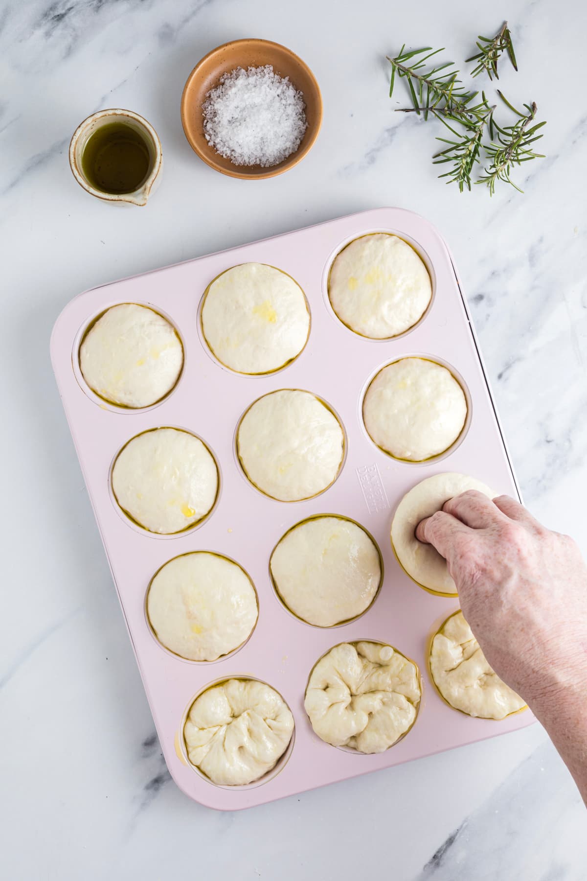 Finger dimpling sourdough focaccia muffin dough before adding olive oil and rosemary.