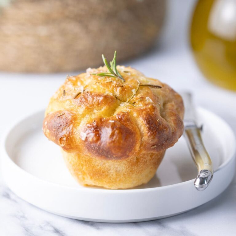 Golden sourdough focaccia muffin baked with olive oil, rosemary and flaky sea salt being served on a plate.