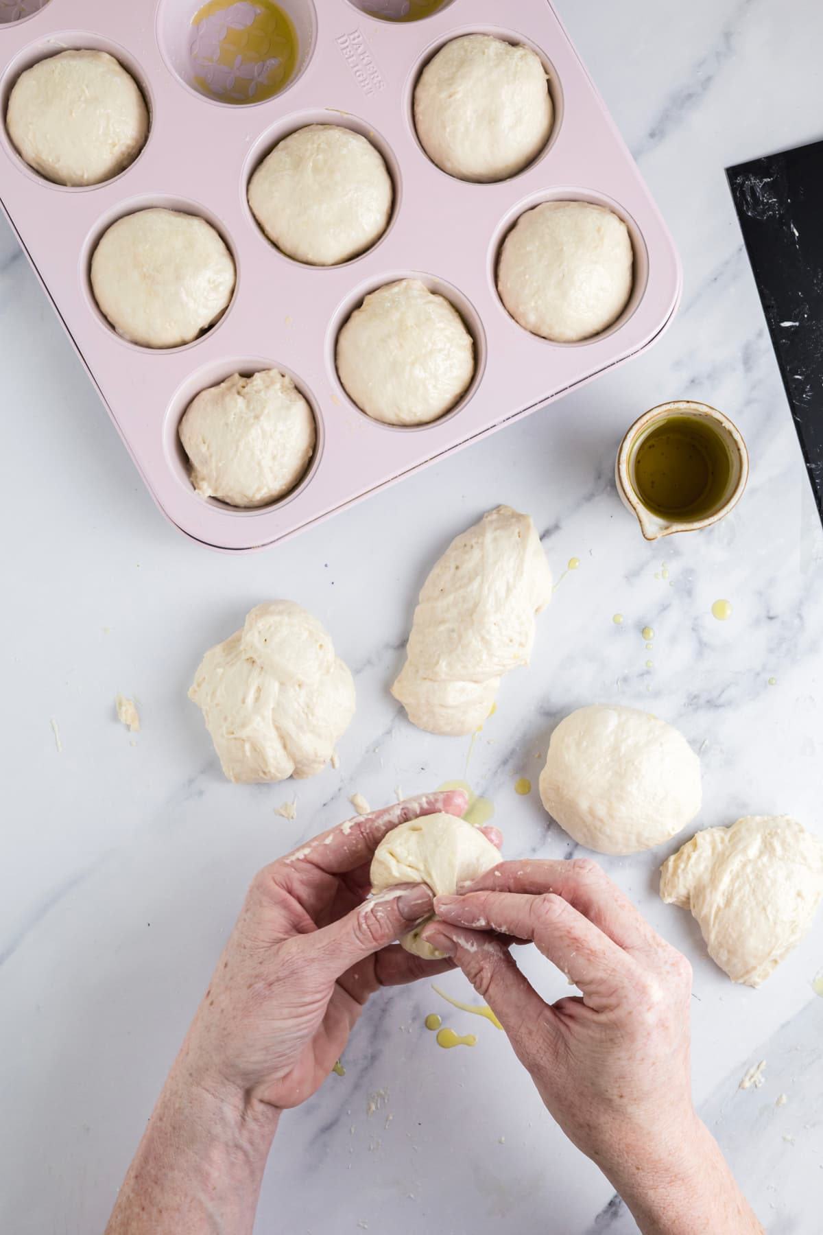 Hands pinching sourdough focaccia muffin dough into a ball before placing it into a muffin pan.