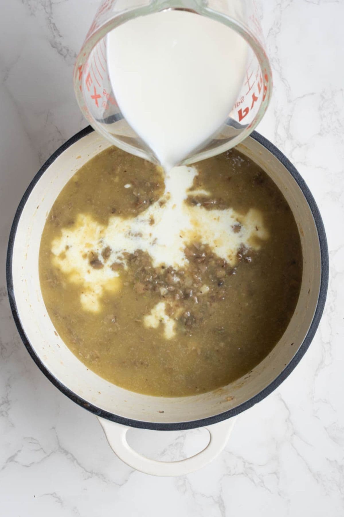 Milk being poured into cooked mushrooms to make creamy mushroom sauce for green bean casserole.