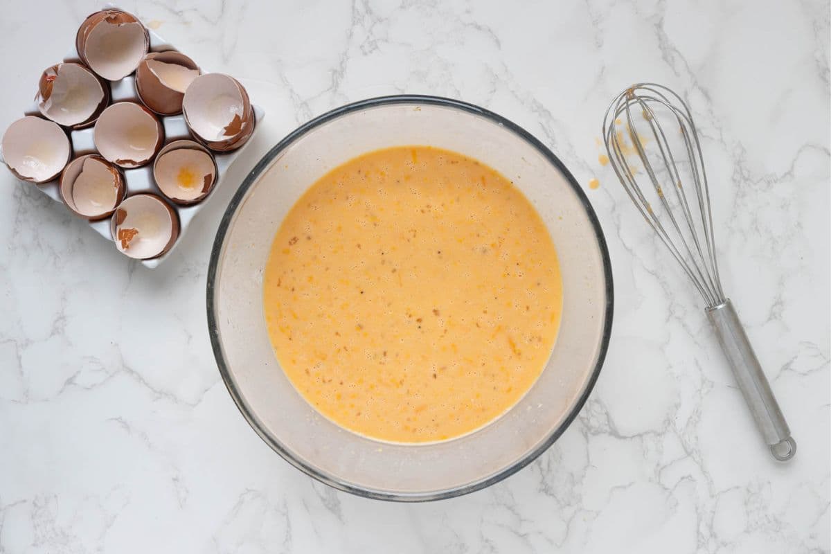 Egg mixture whisked together in a glass bowl for sourdough ham and cheese strata.