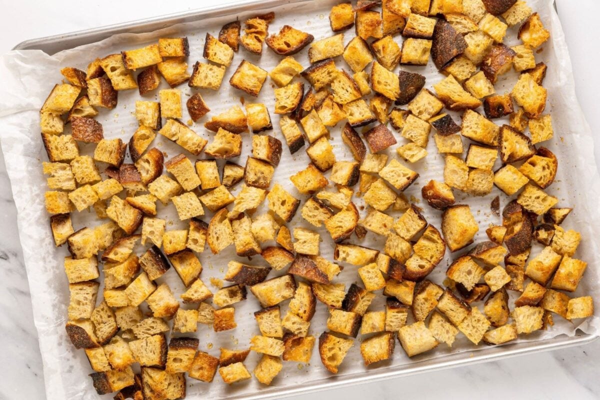 A large baking tray with a single layer of golden brown crispy sourdough croutons that have just been taken out of the oven.