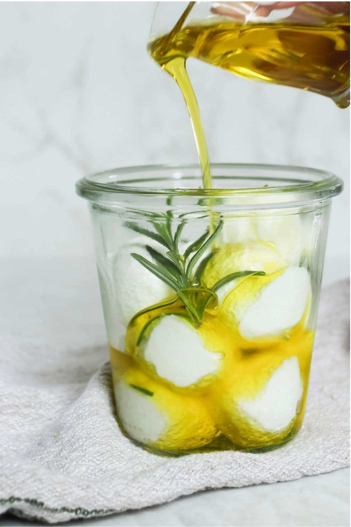 Pouring olive oil over homemade labneh in a glass jar for storage.
