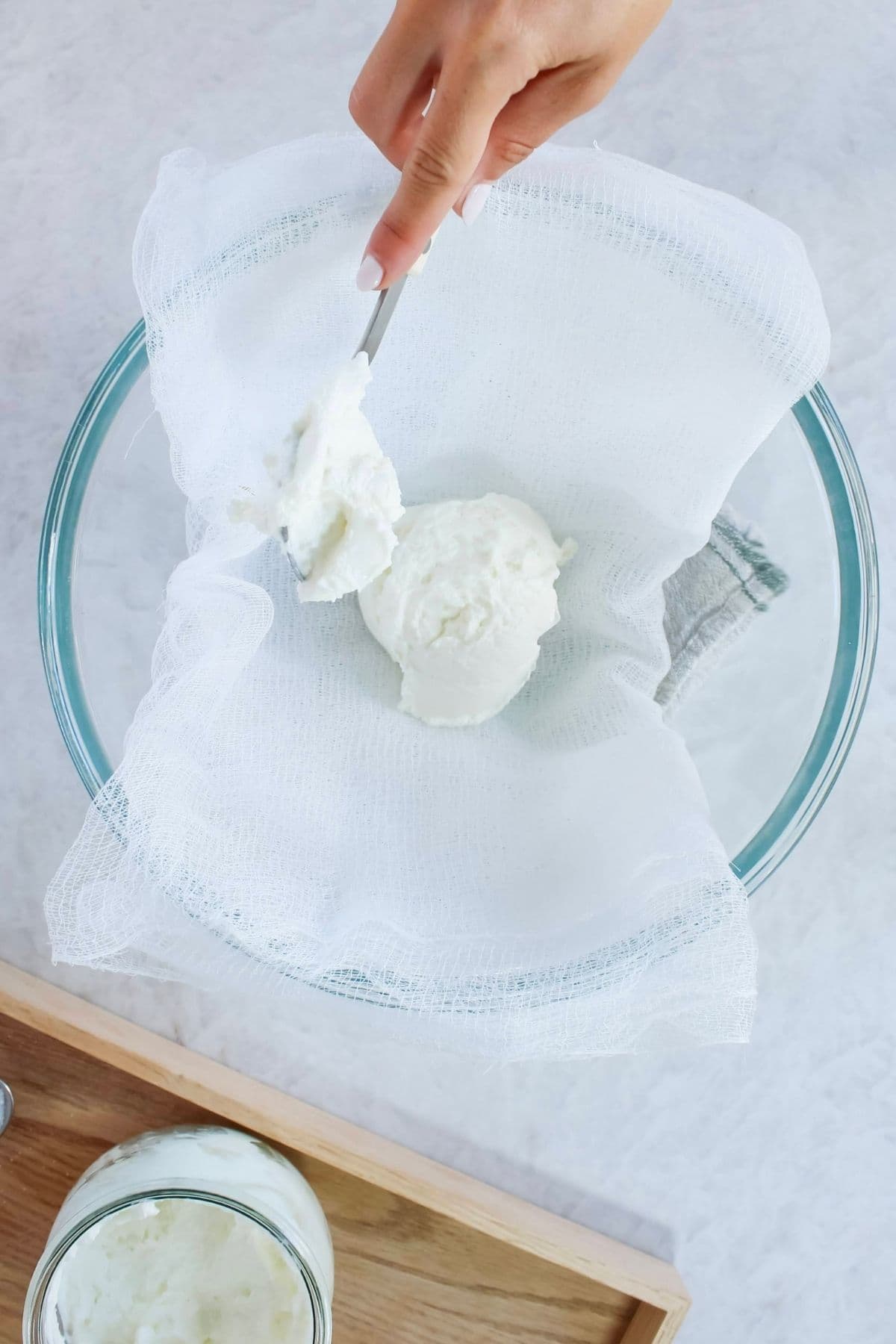 Scooping yogurt onto a cheesecloth to tie up and hang over a bowl to make labneh.