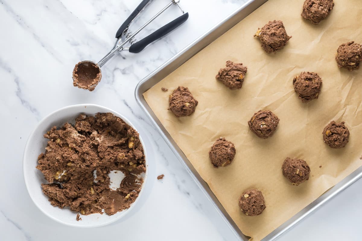 Scoops of sourdough chocolate walnut cookie dough placed onto a parchment-lined baking sheet before baking.