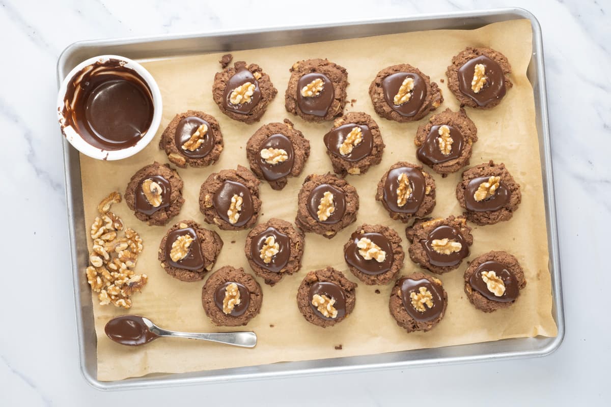 Sourdough chocolate walnut cookies topped with chocolate icing cooling on a parchment-lined baking sheet.