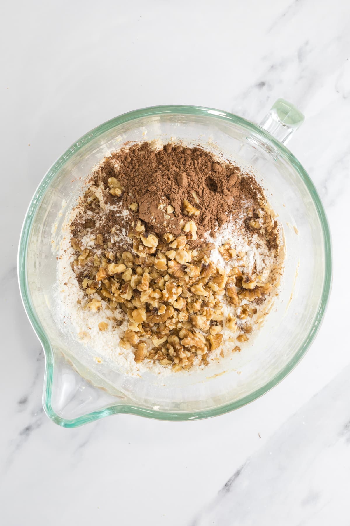 Dry ingredients added on top of the wet ingredients in the mixing bowl for sourdough chocolate walnut cookies.
