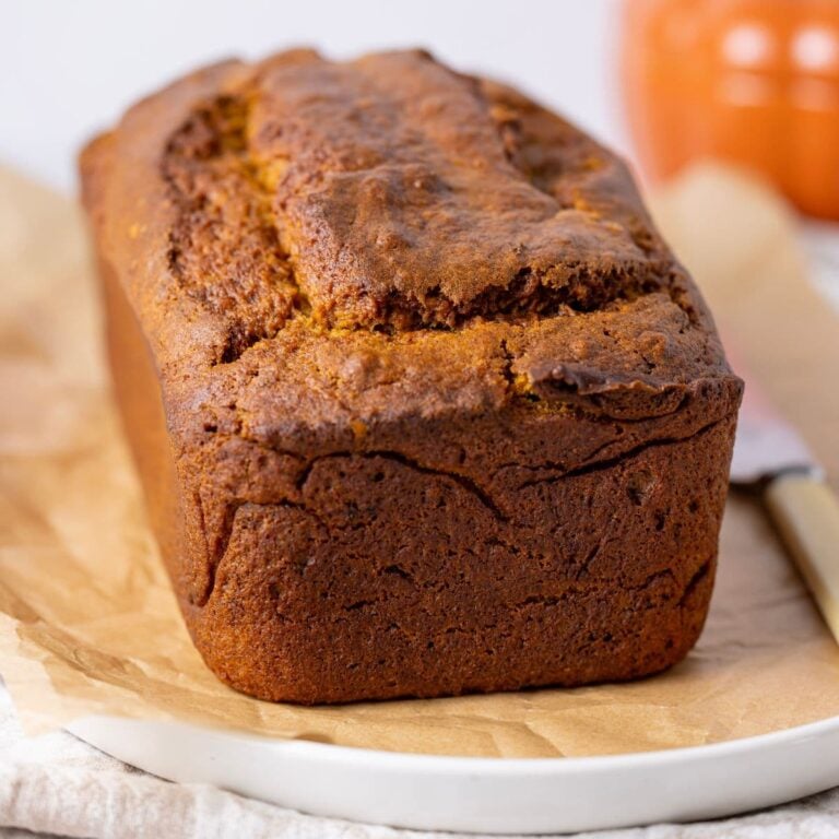 A loaf of sourdough discard pumpkin bread that is freshly baked and sitting on a white platter lined with parchment paper.