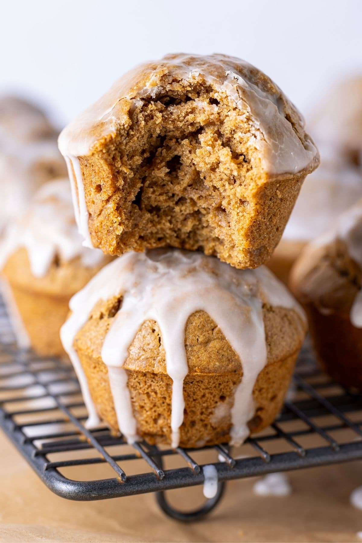 A stack of two sourdough gingerbread muffins drizzled in snowy white glaze. The muffin on top has a bite taken out of it so you can see the tender crumb inside.