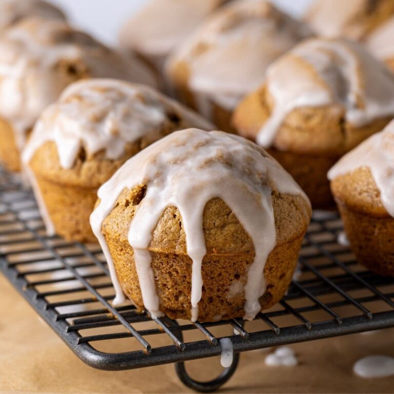 A wire cooling rack holding a batch of sourdough gingerbread muffins that have been drizzled in snowy white icing.