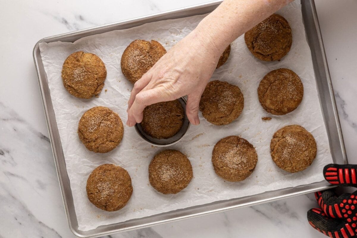A horizontal image showing warm sourdough apple cider cookies that are being swirled with a round biscuit cutter to improve their shape.