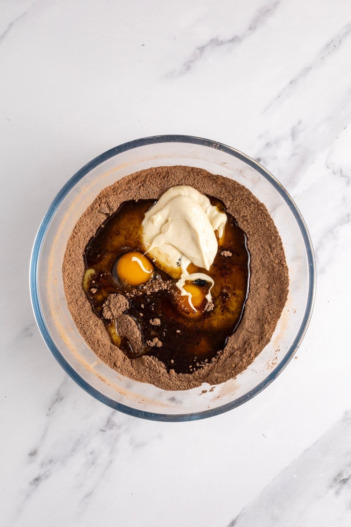A glass bowl showing the wet ingredients for sourdough brownies sitting on top of the dry ingredients.