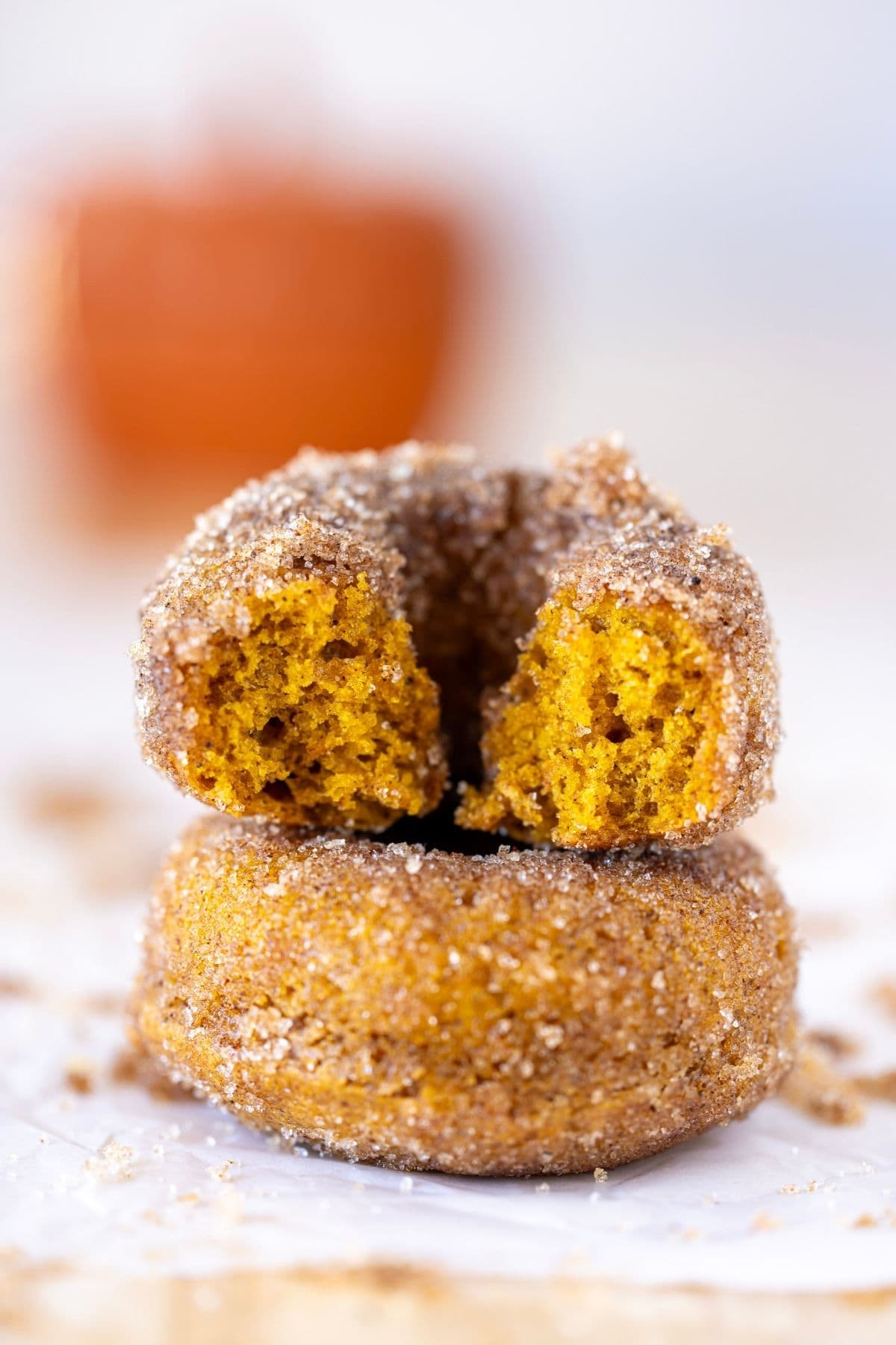 A stack of 2 sourdough discard pumpkin donuts. The donut on top has a bite taken out of it.