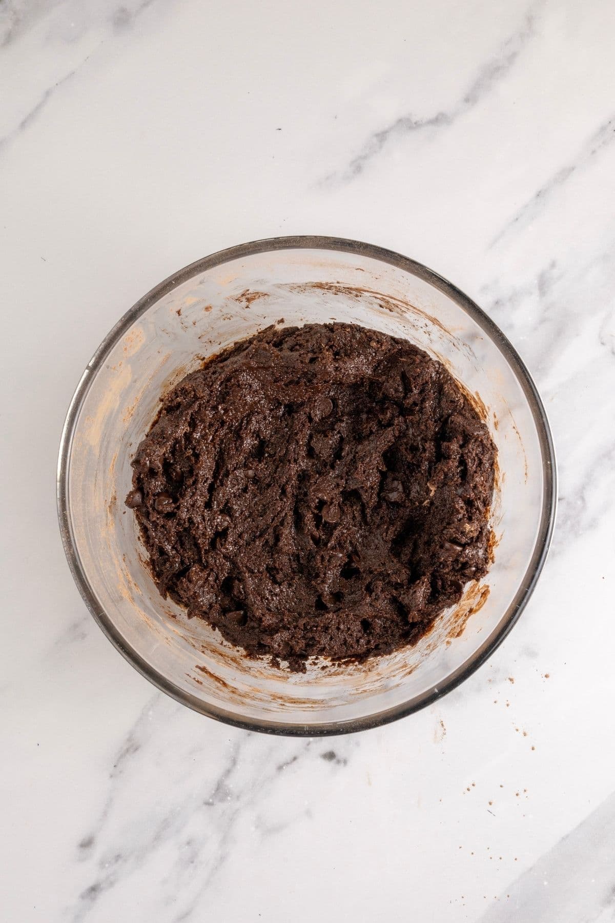 A glass bowl containing the thick brownie batter for a batch of sourdough brownies.