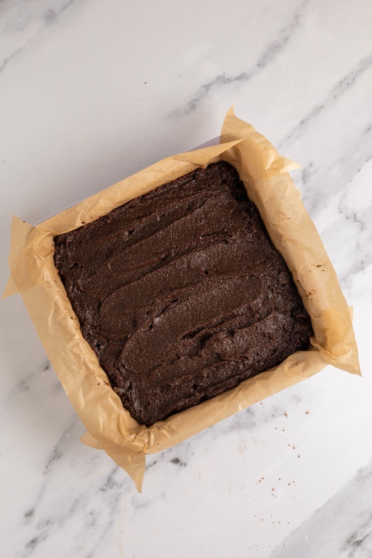 A vertical photo showing the sourdough brownie batter spread into a square pan lined with parchment paper.