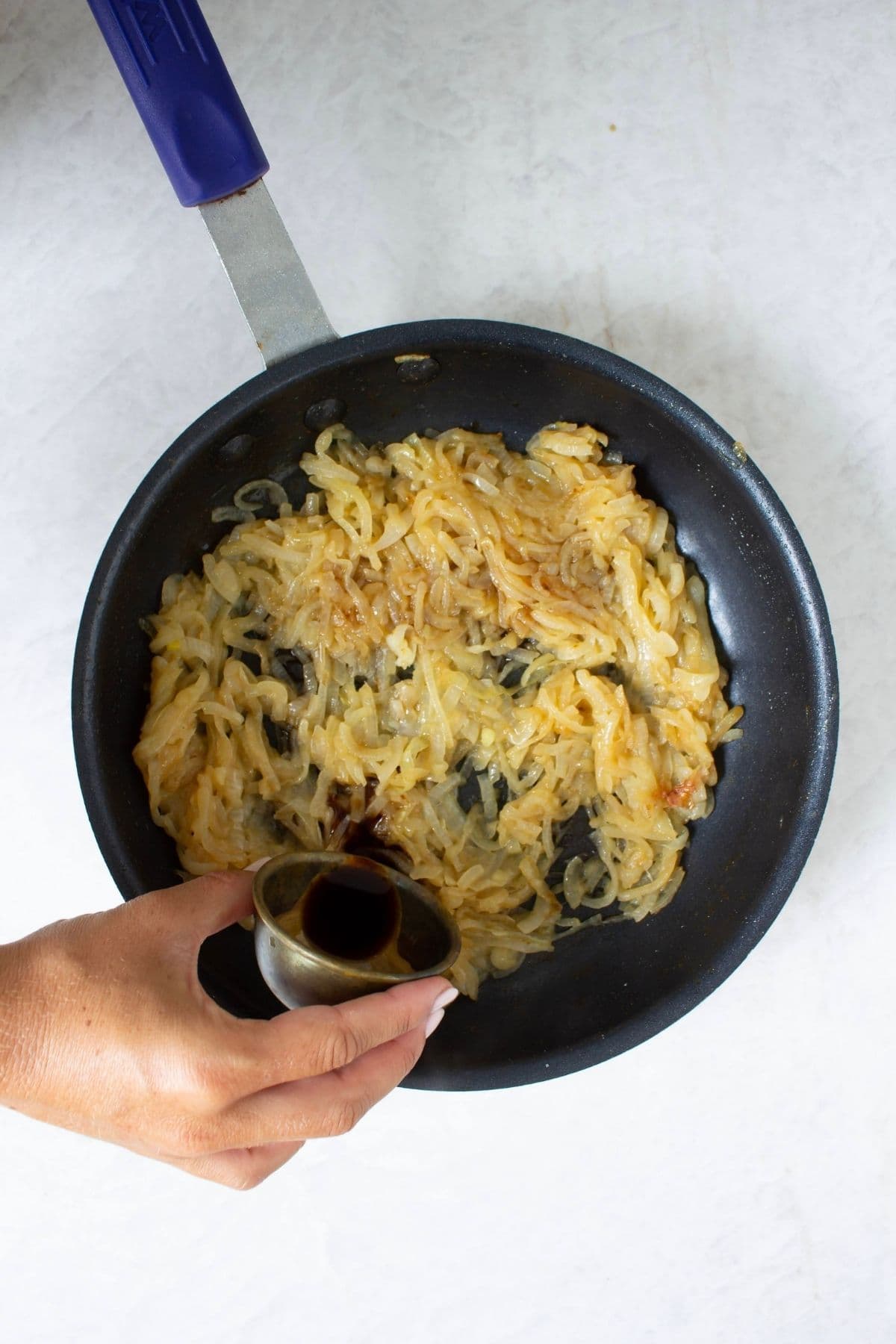 Sliced onions cooking in a skillet as soy sauce is added to make caramelized French onion dip.
