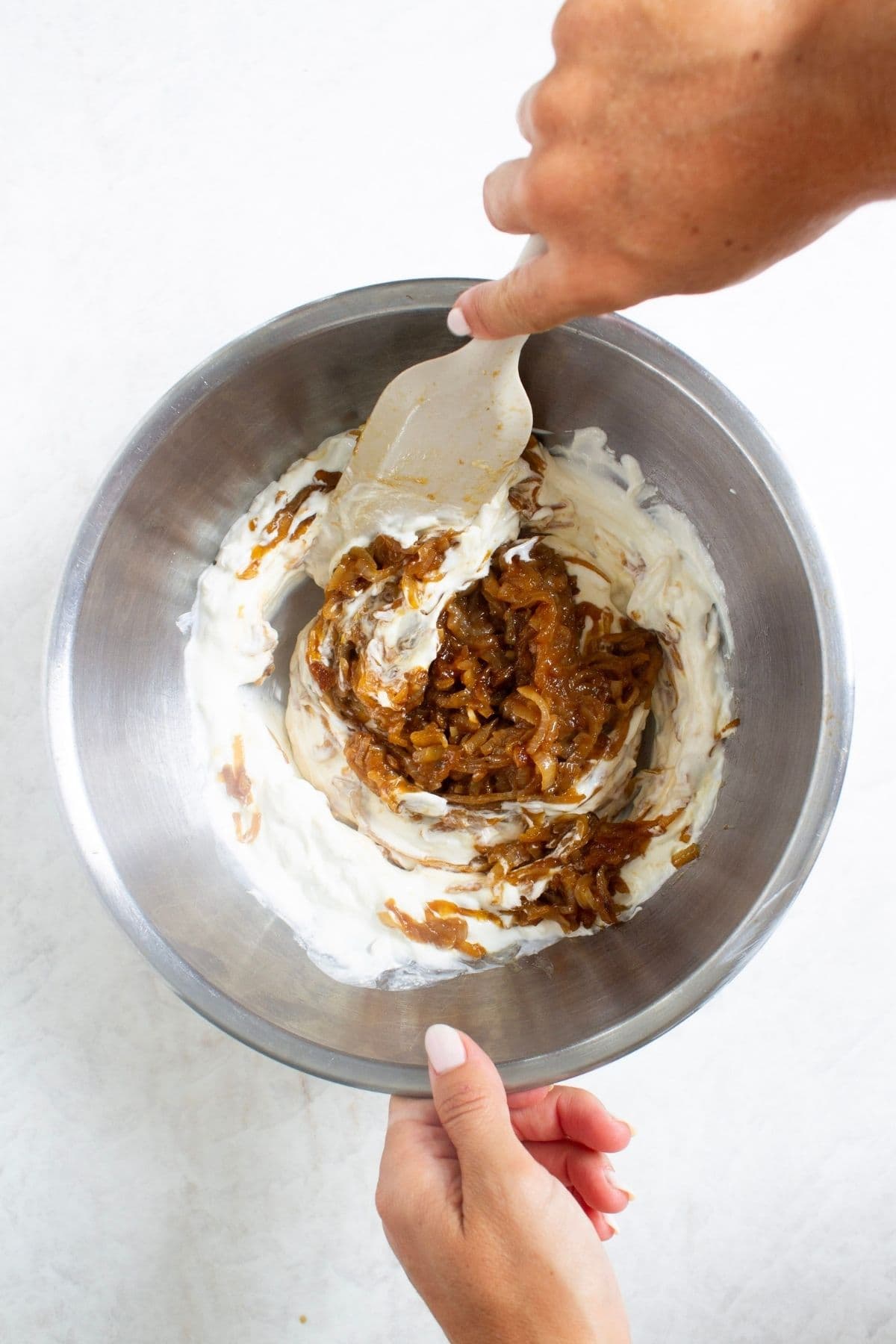 Caramelized onions being folded into the creamy base for homemade French onion dip.