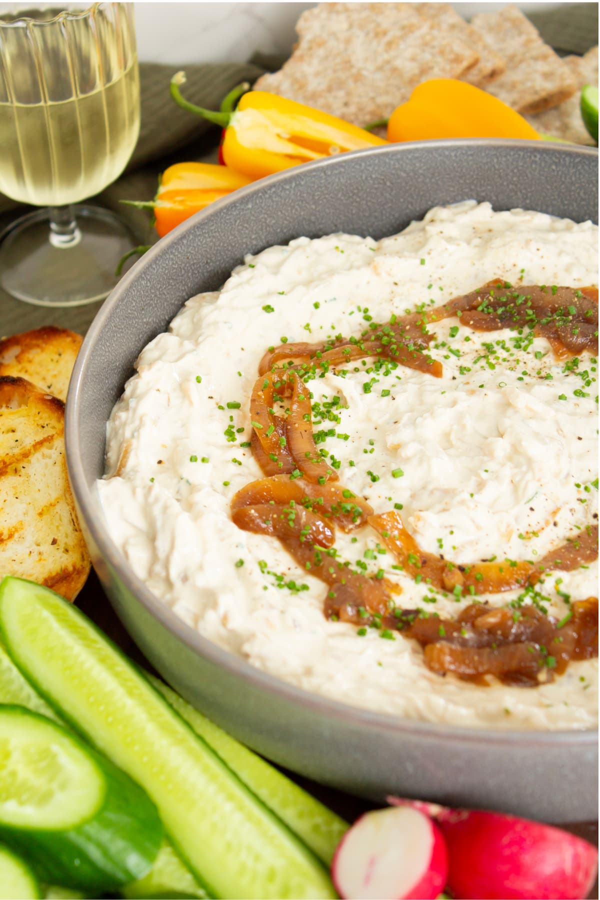 Caramelized French onion dip topped with caramelized onions and fresh chives, served with cucumber, radishes, peppers, and toasted sourdough bread.
