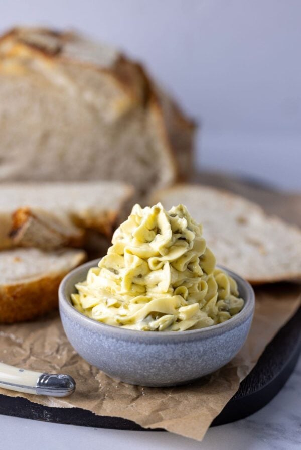 A small grey butter filled with jalapeno honey butter that has been piped into the dish. There is a loaf of sourdough bread in the background.