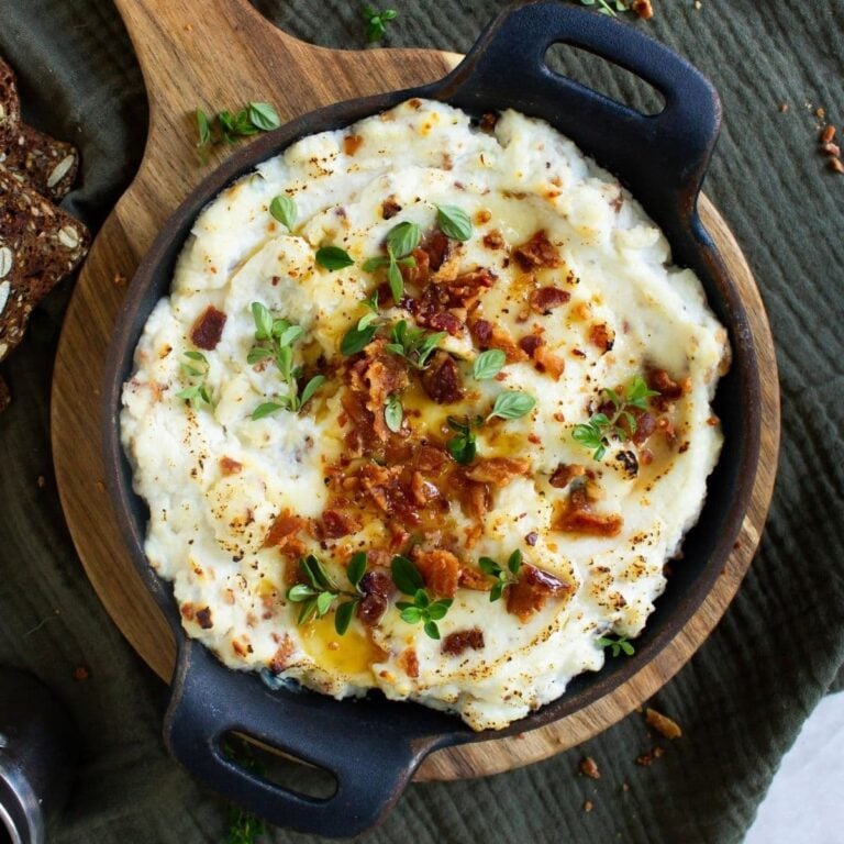 A close up image of maple bacon baked ricotta dip topped with bacon, green onions and a drizzle of maple syrup.