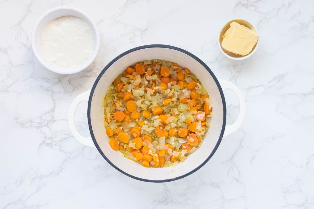 A photo showing the vegetable mixture in the bottom of a large pot. There is a small bowl of sourdough starter and butter next to the pot.