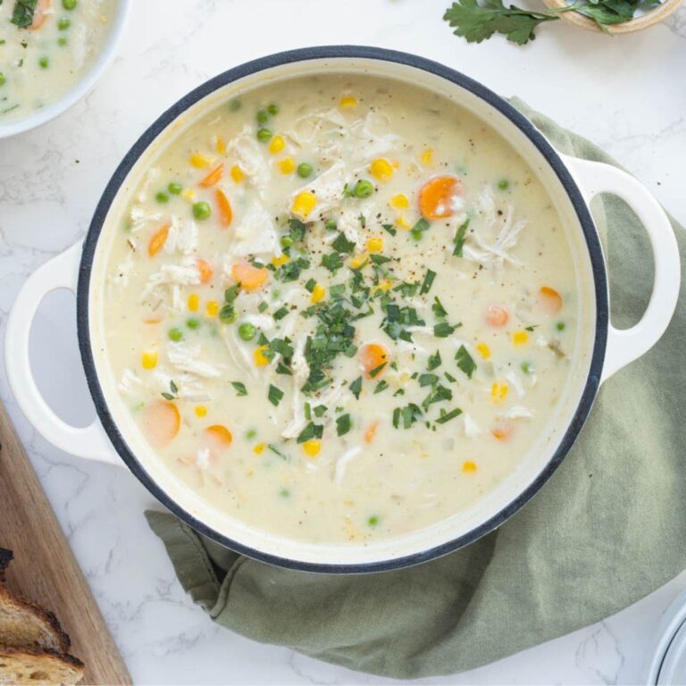 A top down image of a large pot of sourdough chicken pot pie soup. You can see the creamy soup with pops of bright color formed by carrots, peas, corn and flat leaf parsley.