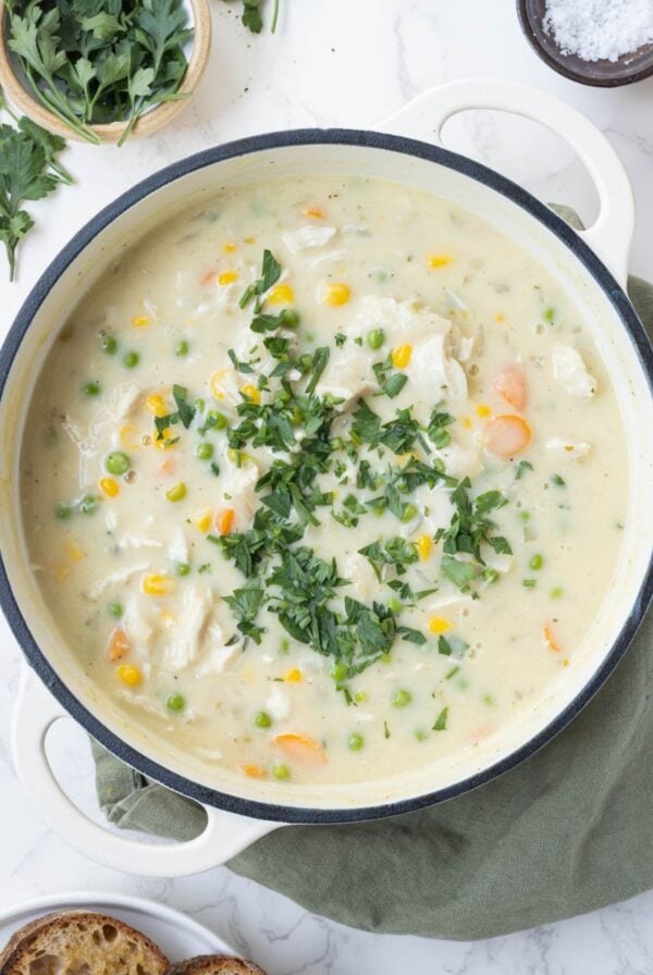 A top down image of a large pot of sourdough chicken pot pie soup. You can see the creamy soup with pops of bright color formed by carrots, peas, corn and flat leaf parsley.